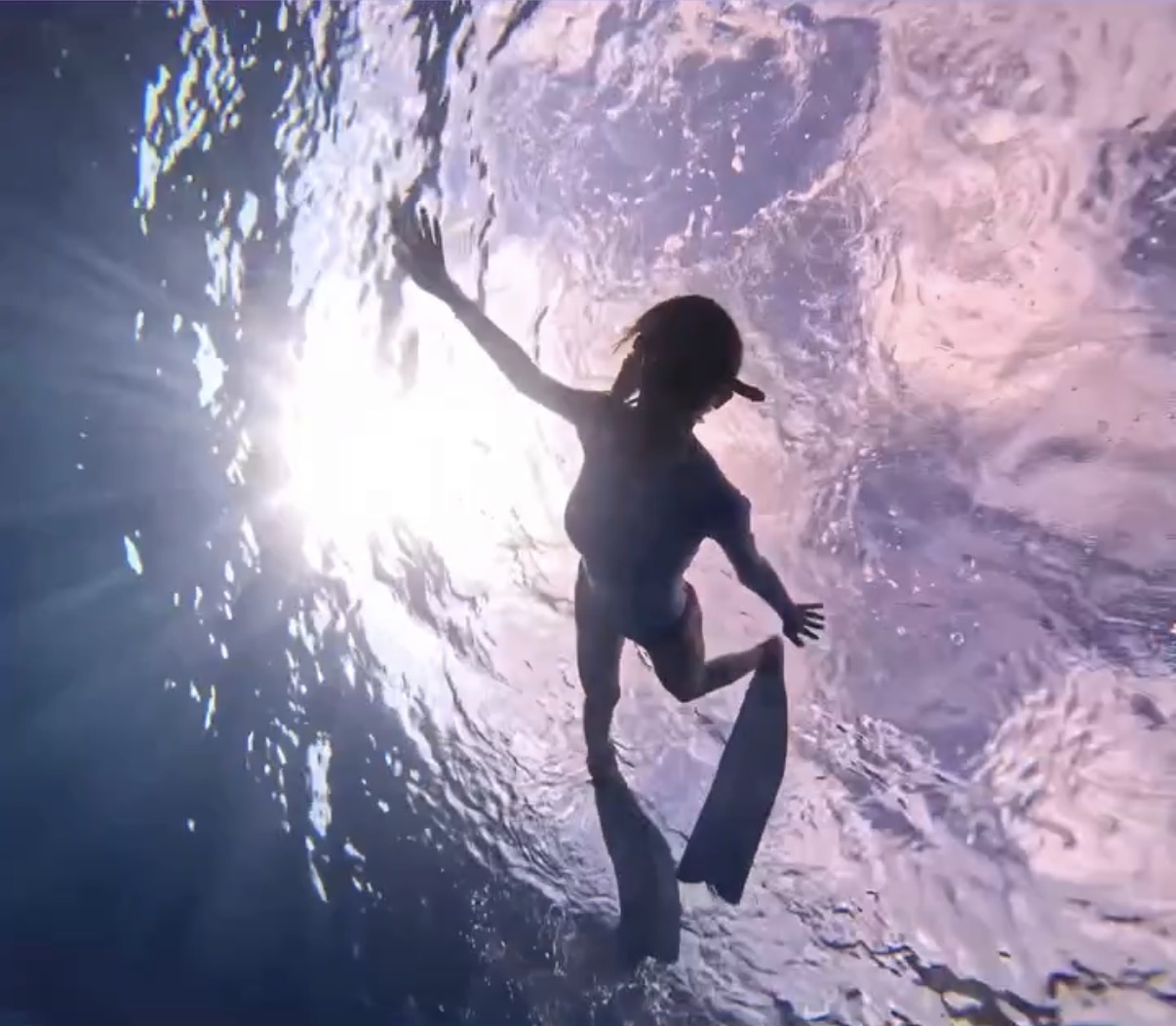 A diver silhouetted beneath the illuminated water surface